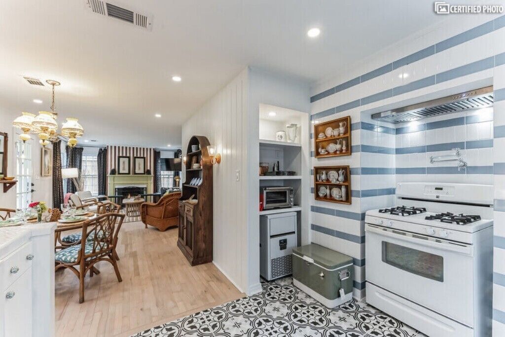 A modern kitchen with striped backsplash, white appliances, and a dining area with wooden furniture.