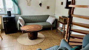 A cozy living room with a green sofa, a round wooden coffee table, and a wooden chair.