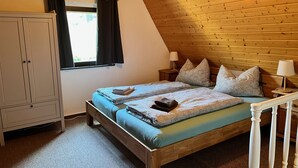 A bedroom with a wooden ceiling, a bed with patterned bedding, a nightstand with a lamp, and a wardrobe.