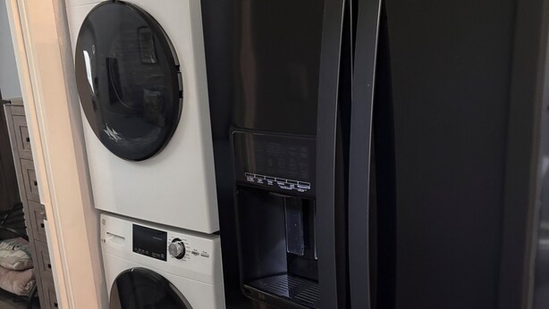 A compact kitchen with a black refrigerator, a washing machine, and a built-in water dispenser.