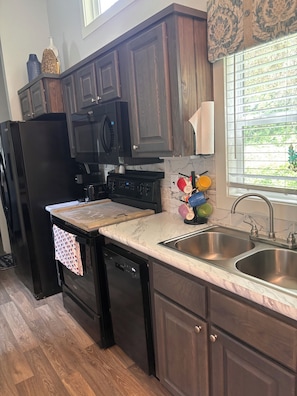 A kitchen with dark wood cabinets, a black refrigerator, a microwave, a stove, and a double sink.
