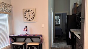 A kitchen with wooden flooring, a clock on the wall, and a table with a flag decoration.