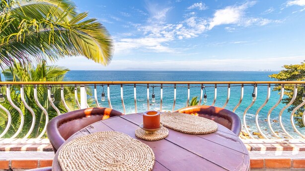 A balcony with a view of the ocean, a table with woven placemats, and a candle.