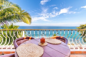 A balcony with a view of the ocean, a table with woven placemats, and a candle.
