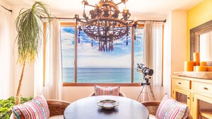 A room with a round table, wicker chairs, a telescope, a large window with a sea view, and a chandelier.