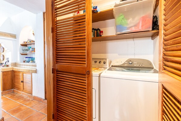 A laundry area with a washing machine, a dryer, and wooden shelves with storage bins.