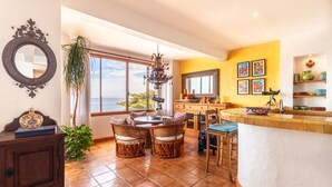 A spacious kitchen with a large island, a dining area with wicker chairs, and a view of the ocean through large windows.