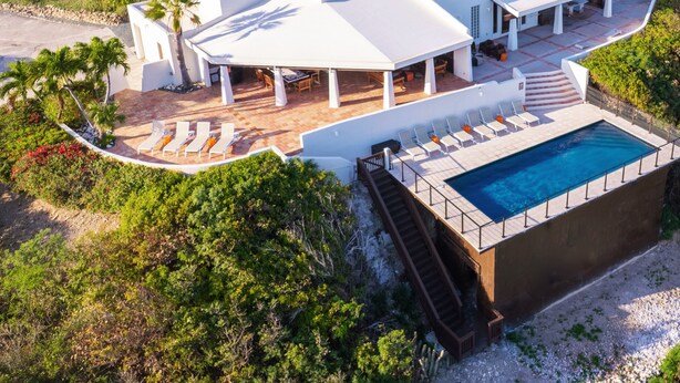 Una casa moderna con piscina, mobiliario de exterior y un porche cubierto.