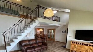 Un vaste espace de vie comprenant un escalier, un canapé en cuir, un pouf et un téléviseur posé sur un meuble en bois.