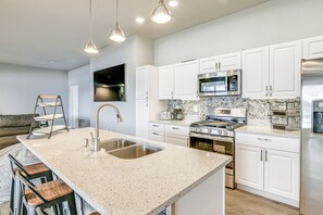 Una cocina moderna con armarios blancos, encimera de granito, electrodomésticos de acero inoxidable y una zona con taburete de bar.