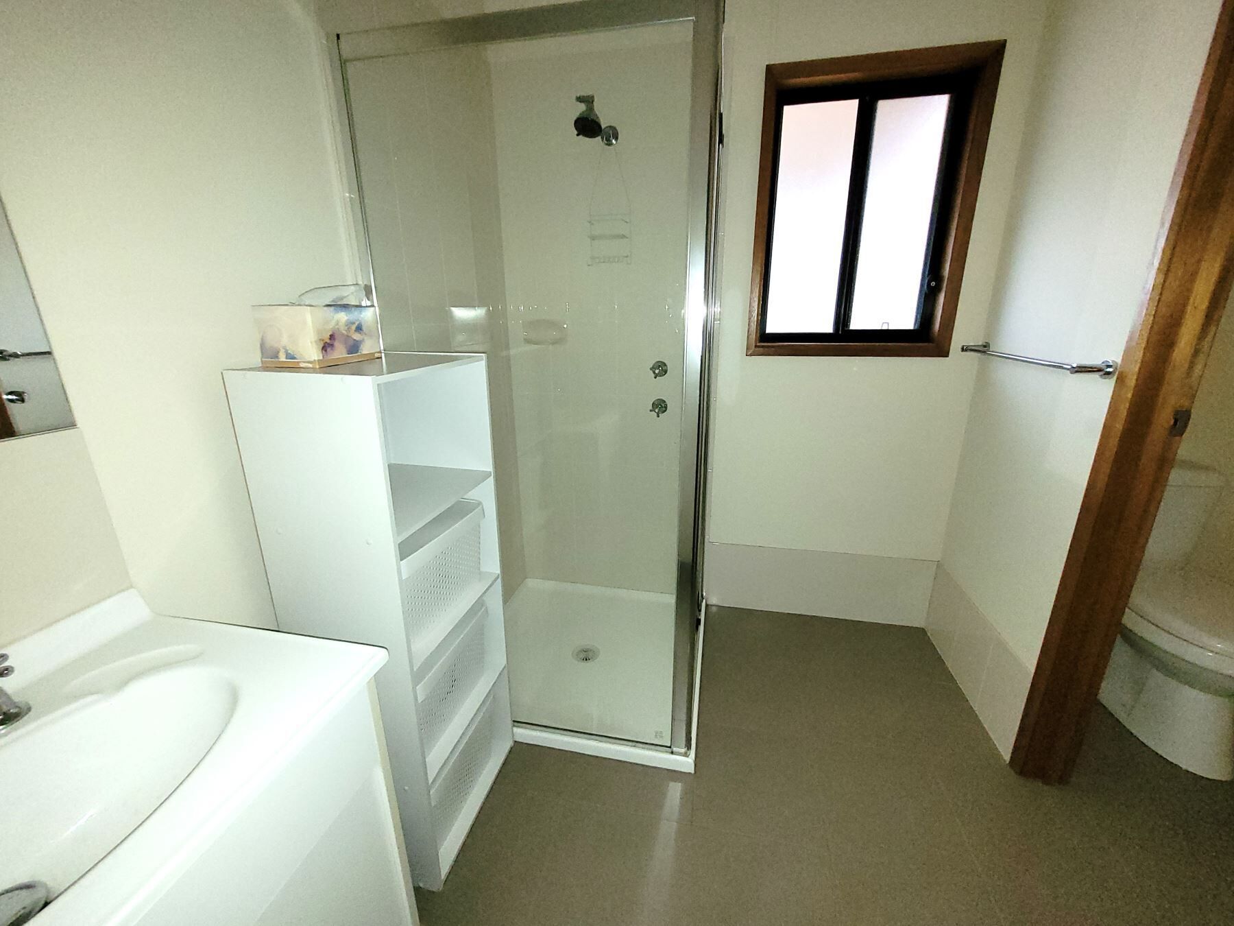 A small, narrow bathroom with a shower, a toilet, and a sink.