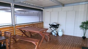 Un espace extérieur abrité avec des tables et des bancs en bois, une poussette et une bouteille de gaz.