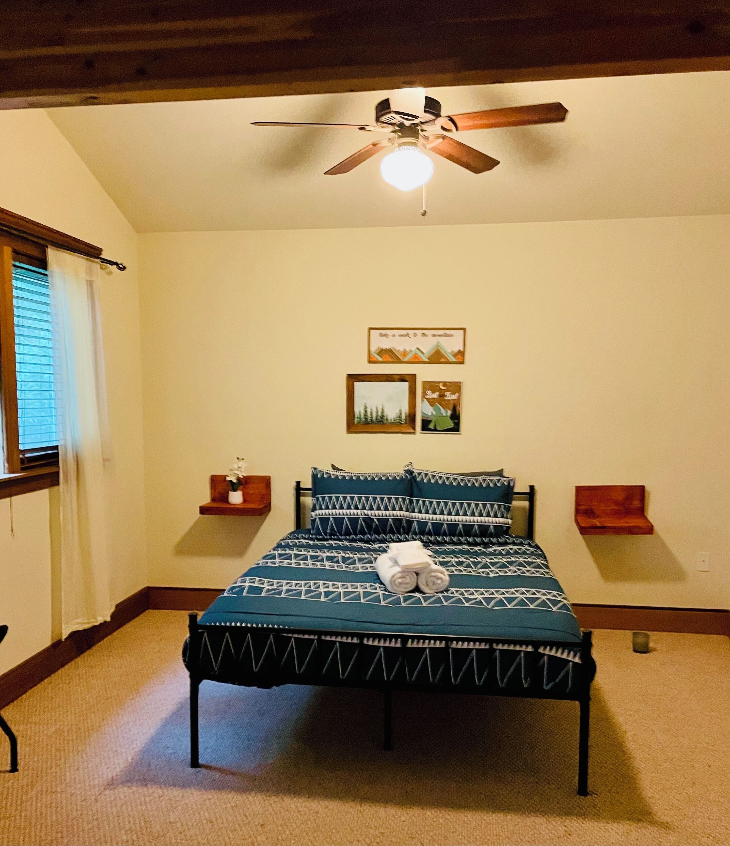 A bedroom with a bed, a ceiling fan, and two wall-mounted side tables.