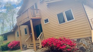 A two-story house with a wooden balcony, a stone foundation, and a front door. - Timber frame chalet with incredible views minutes from Shenandoah National Park. (Linden)