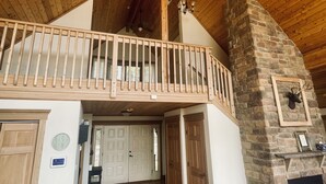 A spacious room with a wooden ceiling, a stone fireplace, and a balcony with wooden railings. - Timber frame chalet with incredible views minutes from Shenandoah National Park. (Linden)