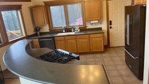 A kitchen with wooden cabinets, a stainless steel refrigerator, a built-in stove, and a window with a view of trees. - Timber frame chalet with incredible views minutes from Shenandoah National Park. (Linden)