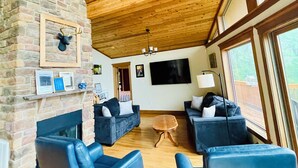 A spacious living area with a stone fireplace, two sofas, and a television mounted on the wall. - Timber frame chalet with incredible views minutes from Shenandoah National Park. (Linden)