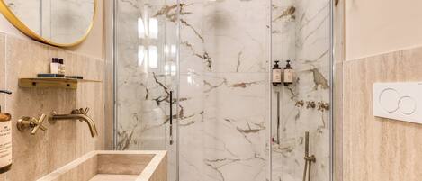 A modern bathroom with a marble shower enclosure, a freestanding bathtub, and a vanity with a mirror.