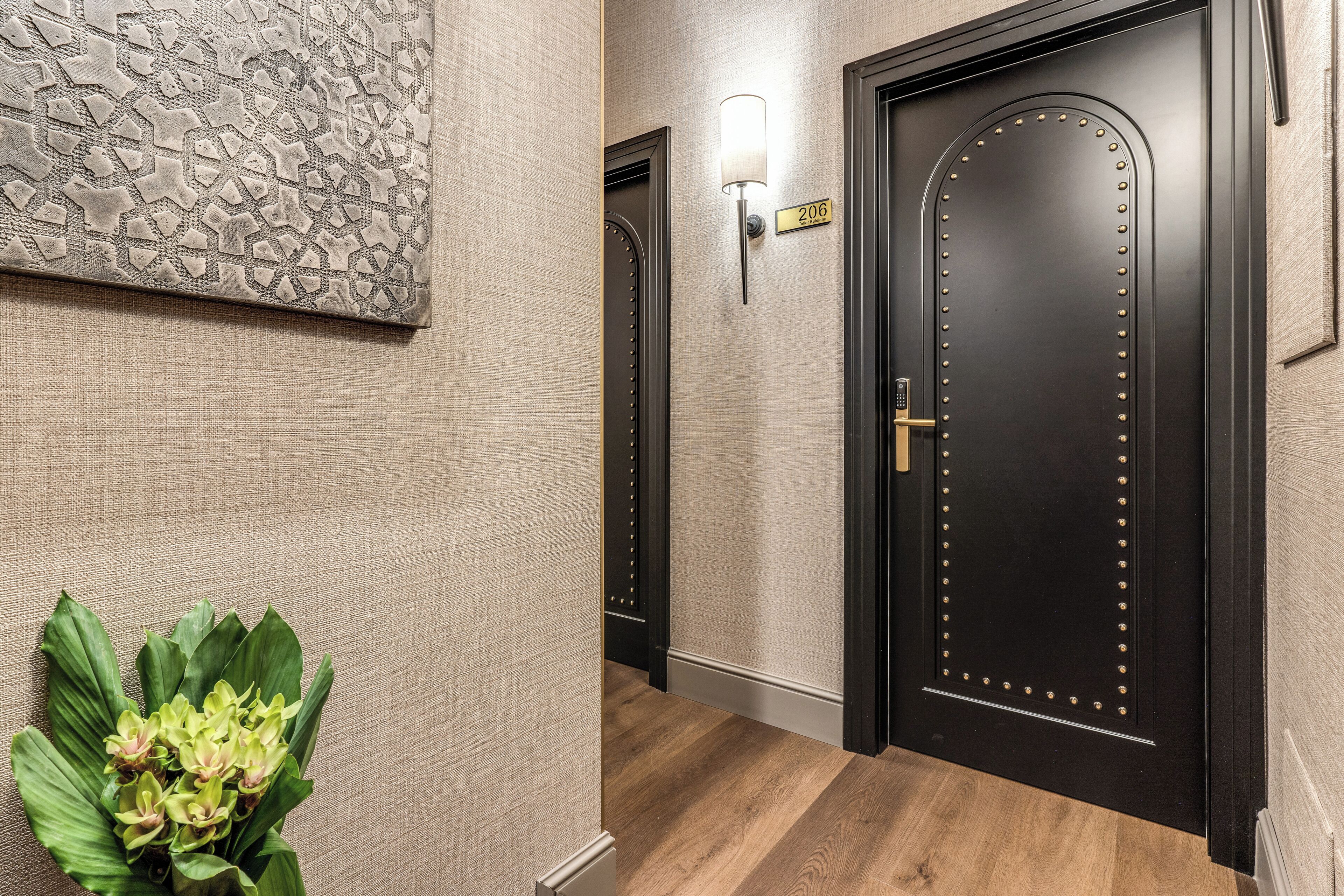 A hallway with a dark wooden door, a wall-mounted light fixture, and a number sign.