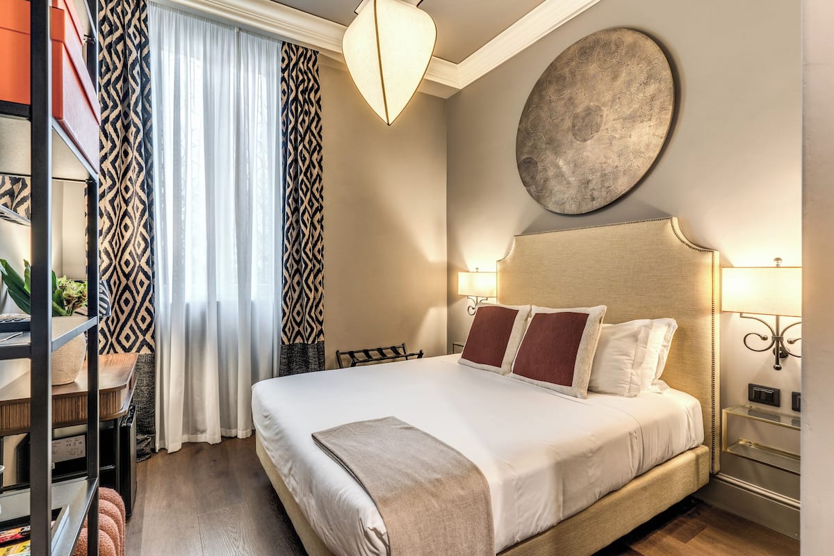 A neatly made bed with a headboard, a bedside table with a lamp, and a large abstract wall art piece.