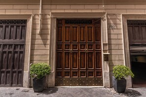 A building entrance with a large wooden door, two potted plants, and a number sign above the door. - Telier Belsiana (Rome)