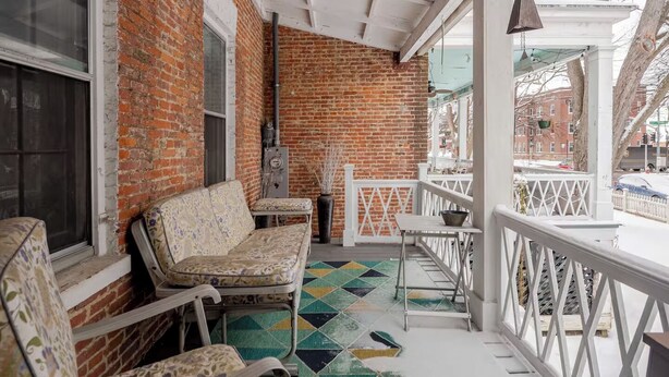 A covered porch with brick walls, a white railing, and a colorful geometric-patterned floor. - Historic Charm Meets Modern Comfort in Downtown Burlington (Burlington)