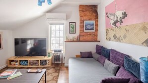 A living room with a TV, sofa, and a brick wall. - Historic Charm Meets Modern Comfort in Downtown Burlington (Burlington)
