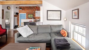 A living room with a grey sofa, a red chair, a wooden coffee table, and a window with a view. - Historic Charm Meets Modern Comfort in Downtown Burlington (Burlington)