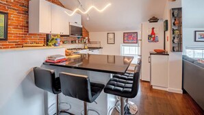 A modern kitchen with a brick wall, white cabinets, a central island, and black bar stools. - Historic Charm Meets Modern Comfort in Downtown Burlington (Burlington)