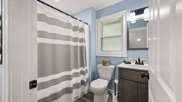 Un baño con cortina de ducha a rayas, un inodoro blanco, un lavamanos con un espejo encima y un armario de madera.