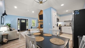 A modern kitchen with white cabinets, a black refrigerator, and a dining area with a dark table and woven placemats. - The Cumberland Collective~The Hideaway~<6mi to lake/golf. Great for families! (Burkesville)