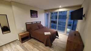 A bedroom with a bed, a nightstand, a mirror, a TV, and a view of a building through large windows. - WTC Suites (Mexico City)