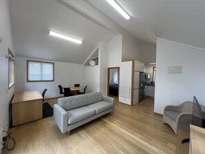 A modern, open-plan living space with a sofa, dining table, and kitchen area. - The Guesthouse, Campbells Bay. (Auckland)