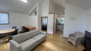 A modern, open-plan living space with a sofa, dining table, and kitchenette. - The Guesthouse, Campbells Bay. (Auckland)