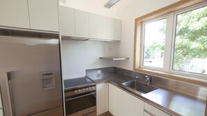 A modern kitchen with stainless steel appliances, white cabinetry, and a window providing natural light. - The Guesthouse, Campbells Bay. (Auckland)