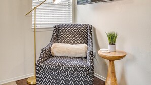 A patterned armchair with a cushion, a floor lamp, and a small wooden table with a potted plant. - Green Door Cutie Close to Everything in The Fort! (Fort Worth)