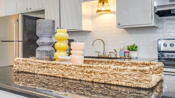 A kitchen with white cabinets, a stainless steel refrigerator, a woven placemat on the counter, and a pendant light above the sink. - Green Door Cutie Close to Everything in The Fort! (Fort Worth)