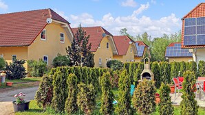 Une rangée de bâtiments jaunes aux toits rouges, dotés de panneaux solaires, et un jardin central agrémenté de haies soigneusement taillées.