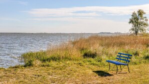 A bench by a lake with tall grass and a tree in the background. - Ferienwohnung Bodstedt (Bodstedt)