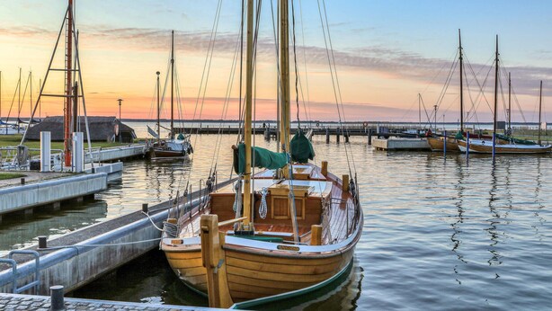 A wooden boat docked at a marina with other boats, a pier, and a sunset in the background. - Ferienwohnung Bodstedt (Bodstedt)