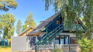 A wooden cabin with a steep staircase, a fenced yard, and a clear blue sky. - Ferienwohnung Bodstedt (Bodstedt)