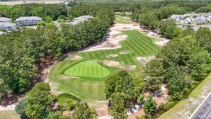 Een golfbaan met een verzorgd fairway, zandbunkers en een putting green, omgeven door dichte bomen en woongebouwen.