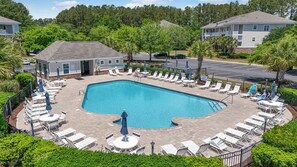 A rectangular pool with lounge chairs and umbrellas arranged around it, surrounded by greenery and a building with a porch. - 3BR Barefoot Resort Condo in North Myrtle Beach! 🐕 Dog Stays FREE (North Myrtle Beach)