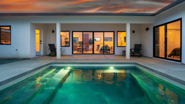 A modern house with a swimming pool, large glass doors leading to a patio, and a sunset view. - Hoku House - Heated Pool/Spa - Luxury Walkable Oasis in Downtown Joshua Tree (Joshua Tree)
