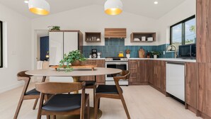 A modern kitchen with wooden cabinets, a round dining table, and two pendant lights. - Hoku House - Heated Pool/Spa - Luxury Walkable Oasis in Downtown Joshua Tree (Joshua Tree)