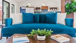 A modern living room with a teal sofa, white cushions, a wooden coffee table, and a potted plant. - Hoku House - Heated Pool/Spa - Luxury Walkable Oasis in Downtown Joshua Tree (Joshua Tree)