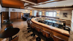 A spacious bar area with a curved counter, multiple bar stools, and a fireplace. - The Lodge Luxury Suites (Hancock)