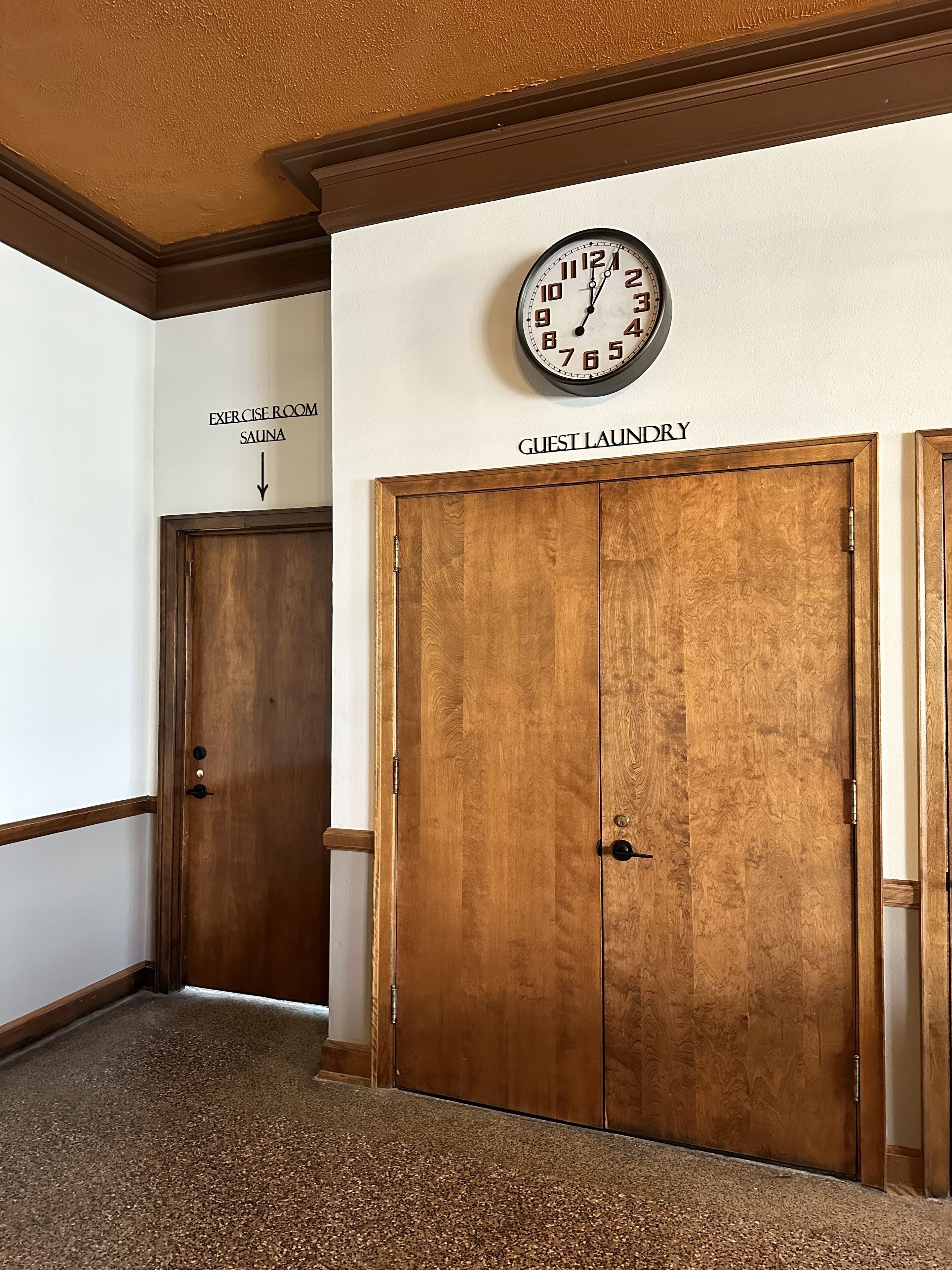 A hallway with a clock, a sign for the exercise room and sauna, and a guest laundry door.