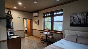 A bedroom with a bed, a desk, and a chair. There is a window with a view of the outside. - The Lodge Luxury Suites (Hancock)
