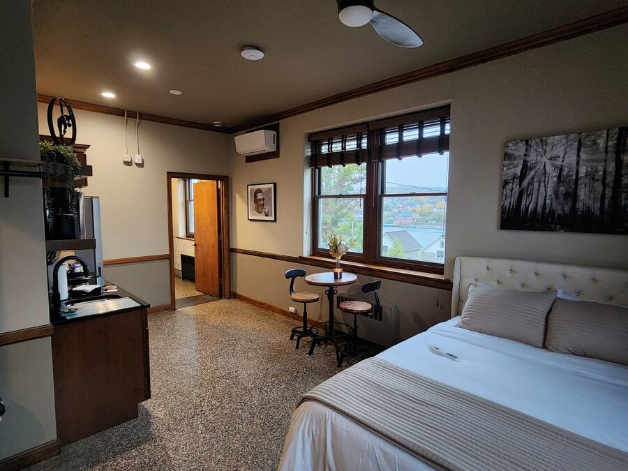 Quarto com cama, escrivaninha e cadeira. Há uma janela com vista para o exterior.
